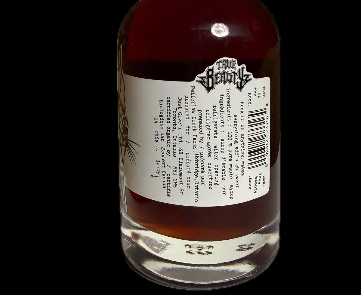 A bottle of amber liquid, maple syrup, with a black cap and a white label showing the back text, set against a solid black background.